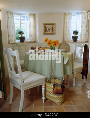 Meuble blanc-couvre sur des chaises blanches à table circulaire avec un chiffon blanc vert pâle en cottage salle à manger avec sol Banque D'Images