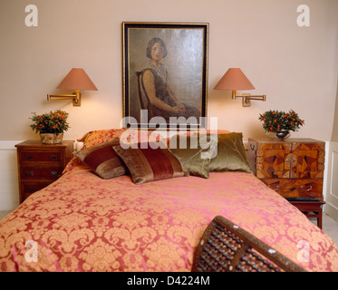 Mur éclairé-lampes et portrait à l'huile au-dessus de lit avec couette en soie damassée rouge et coussins en appartement chambres Banque D'Images