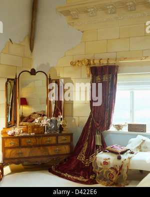 Coiffeuse ancienne avec miroir triple dans chambre avec rideau rouge et trompe- l'oeil peinture murale en pierre d'effet sur les murs Banque D'Images