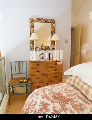 Miroir Floral au-dessus de la poitrine de pin-de-tiroirs avec lampes blanches dans la petite chambre avec toile rose-de-Jouy couette sur le lit Banque D'Images