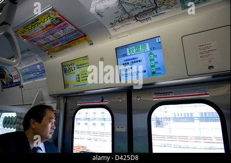 Businessman pairs hors de la fenêtre de la ligne Yamanote line de Tokyo boucle train. Le prochain arrêt est Akihabara comme indiqué sur l'écran de télévision. Banque D'Images