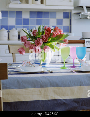 Close-up de la verseuse de tulipes roses sur la table avec un chiffon bleu +blanc et pastel wineglasses dans cuisine côtière Banque D'Images