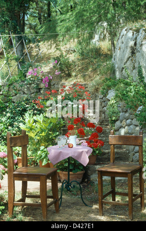 Chaises en bois simple à table en métal avec un chiffon rose sur la petite terrasse toscane ombragé ci-dessous marches de pierre à Hillside Garden Banque D'Images