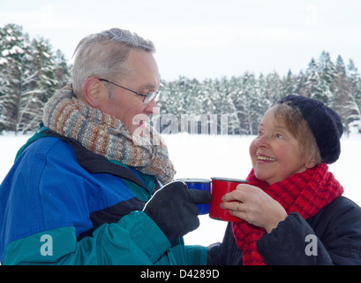 Personnes âgées heureux couple toasting with tasses de boissons chaudes, à l'extérieur en hiver neige paysage de forêt Banque D'Images