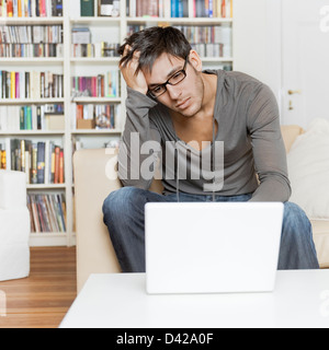 L'homme à l'aise à la maison en utilisant son ordinateur portable pour surfer sur internet et faire tout sorte d'internet. Banque D'Images