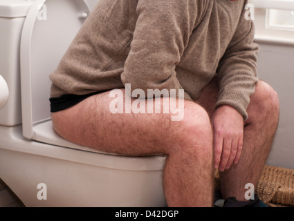 Homme assis sur les toilettes avec son pantalon vers le bas Banque D'Images