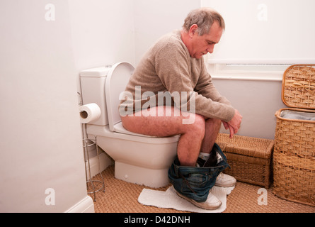 Homme assis sur les toilettes avec son pantalon vers le bas Banque D'Images