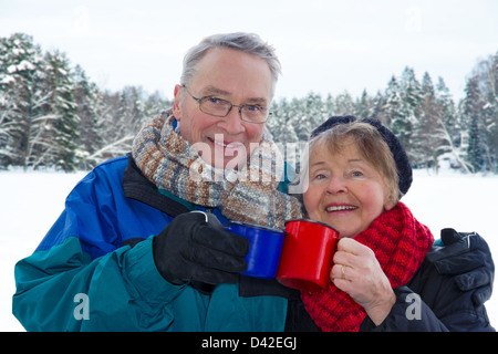 Senior couple Smiling attractive à l'extérieur en hiver neige paysage, holding de boissons chaudes tasses Banque D'Images
