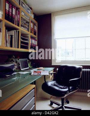 Fauteuil pivotant en cuir noir recouvert de verre au bureau avec un ordinateur portable dans l'étude avec fort fichiers sur tablettes murales Banque D'Images