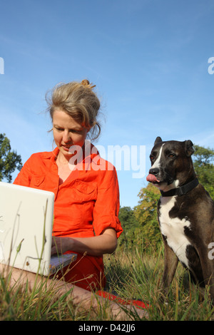 Berlin, Allemagne, une femme assise avec son ordinateur portable sur la pelouse, à côté de son chien Banque D'Images