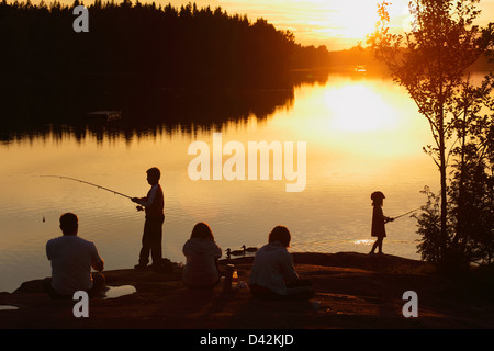 Silvkoparen, Suède, une famille s'assied sur le bord d'un lac au coucher du soleil Banque D'Images