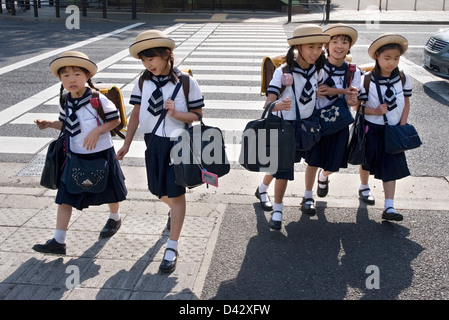 L'école élémentaire de cinq jeunes filles en uniforme de marin et mignon chapeau de traverser la rue sur le chemin du retour de l'école de Tokyo. Banque D'Images