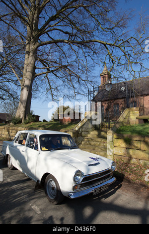 Village de Coddington, Angleterre. Vue pittoresque sur un livre blanc 1967 Mk1 Ford Cortina GT en passant par le village de Coddington. Banque D'Images