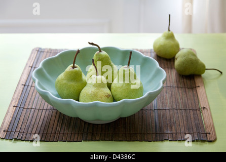 6 Les poires dans un plat festonné bleu sur un tapis de bambou et green table Banque D'Images