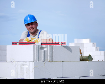 Mason portant des casques bleus posant reposant sur un mur de bloc blanc sur ciel bleu Banque D'Images