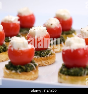 Fingerfood faits de pain grillé, tomates cerises, Pesto au basilic rempli de mozzarella, surmontée d'assaisonnement et le Parmesan reggiano. Banque D'Images