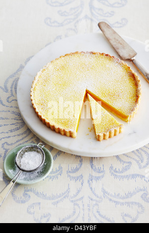 Tarte au citron sur un socle de marbre avec pelle à tarte et bol de sucre glace sur table en Studio Banque D'Images