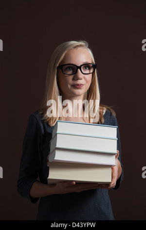 Portrait de Blond, Teenage Gril portant des lunettes et de l'exécution de la pile de livres, Studio Shot sur fond noir Banque D'Images