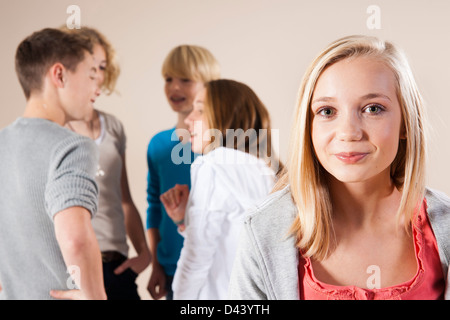 Portrait de Blond, Teenage Girl Smiling at Camera avec groupe de jeunes garçons et filles de parler en arrière-plan, fond blanc Banque D'Images