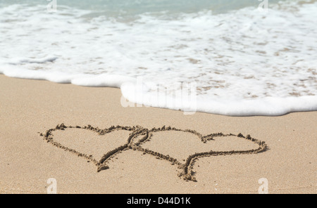 Cœurs liés dessiné dans le sable sur une plage tropicale par ocean surf - love holiday vacation romance concept Banque D'Images