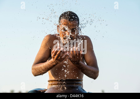 L'homme indien aux projections d'eau sur lui-même à partir d'un pot d'eau au coucher du soleil. L'Inde Banque D'Images