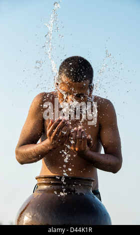 L'homme indien aux projections d'eau sur lui-même à partir d'un pot d'eau au coucher du soleil. L'Inde Banque D'Images