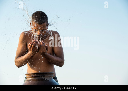 L'homme indien aux projections d'eau sur lui-même à partir d'un pot d'eau au coucher du soleil. L'Inde Banque D'Images