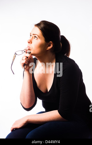 Une jeune femme, les cheveux bruns, assise seule, à la triste bas enfoncé lonely UK holding lunettes lunettes assis Banque D'Images