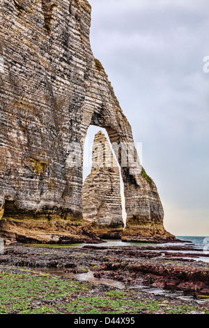 Falaises d'Etretat dans le pays de la région du nord de la France : un rocher de l'Aiguille vue à travers une arche naturelle lors de la marée basse. Banque D'Images