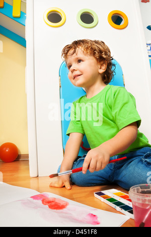 Garçon de deux ans avec peinture aquarelles assis sur le plancher dans chambre d'enfant Banque D'Images