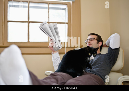 Homme détendue avec des lunettes se lit le papier avec Chat Banque D'Images