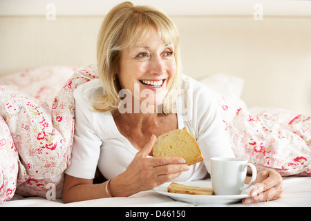 Senior Woman se blottit sous couette Eating Breakfast Banque D'Images