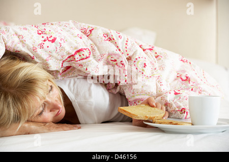 Senior Woman se blottit sous couette Eating Breakfast Banque D'Images