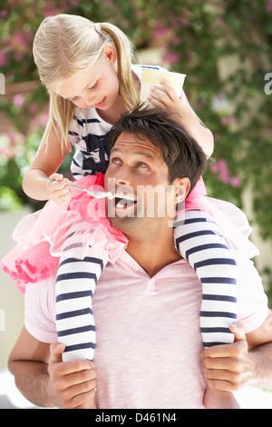 Father Giving Daughter Ride sur les épaules à l'extérieur tout en mangeant des guimauves Banque D'Images