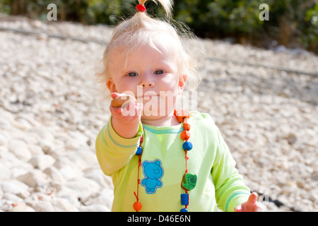 Cute baby girl holding out un caillou à jouer. Banque D'Images