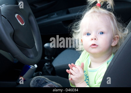 Petite fille assise sur le siège du conducteur dans une voiture familiale. Banque D'Images