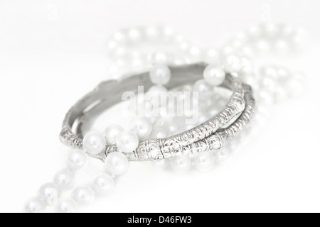 Un ensemble d'accessoires composé de deux bracelets en argent et perles imitation sur blanc. Banque D'Images