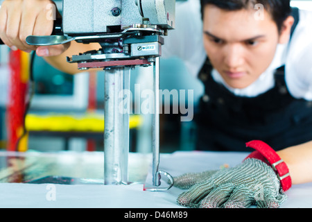 À l'aide d'un travailleur cutter - une grande machine pour couper les tissus en question- dans une usine de textiles chinois, il porte un gant de chaîne Banque D'Images