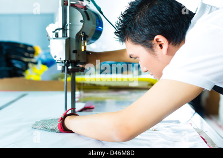 À l'aide d'un travailleur cutter - une grande machine pour couper les tissus en question- dans une usine de textiles chinois, il porte un gant de chaîne Banque D'Images