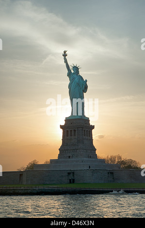 La Statue de la liberté qui se profile par une brillante le coucher du soleil.. Banque D'Images