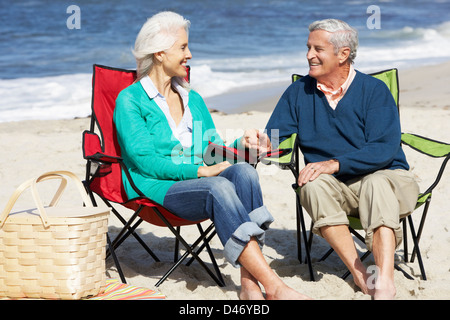 Senior Couple Sitting on beach in transats Having Picnic Banque D'Images