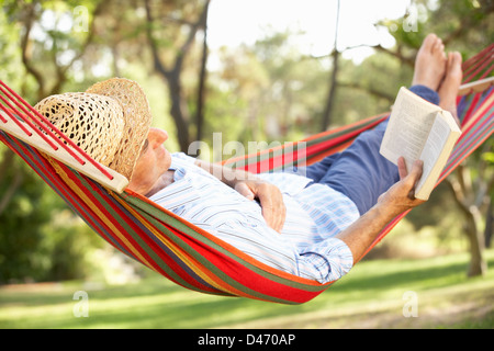 Senior Woman Relaxing In Hammock With Book Banque D'Images