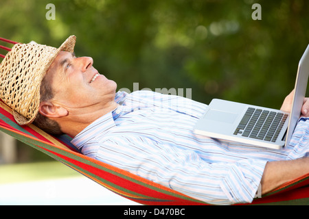 Senior Man Relaxing In Hammock With Laptop Banque D'Images