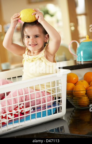 Fille assise dans le panier de Blanchisserie sur comptoir de la cuisine avec du citron Banque D'Images