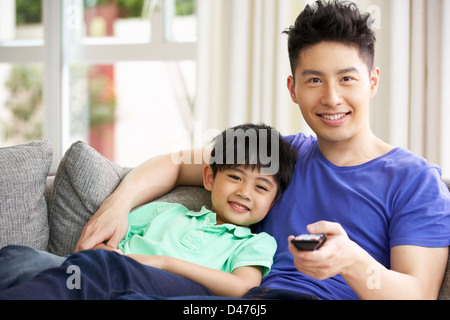 Père et fils chinois assis et regarder la télé sur canapé ensemble Banque D'Images