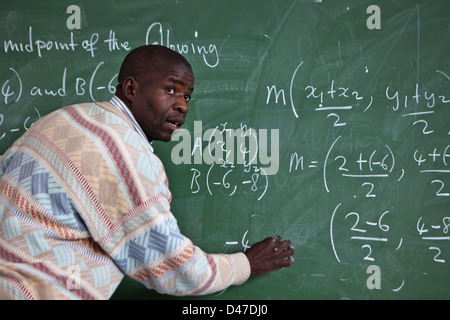 Un enseignant de l'école d'Afrique du Sud examine sa classe comme il l'écrit une équation mathématique sur le tableau noir. Cape Town, Afrique du Sud. Banque D'Images