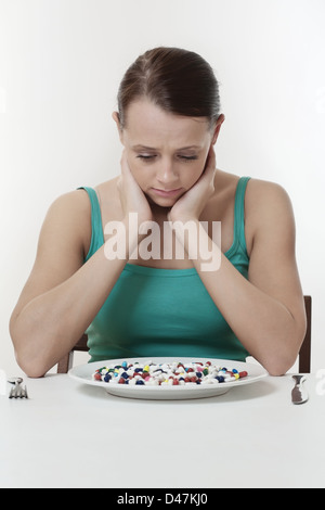 Femme assise à une table sur le point de manger une assiette pleine de pilules Banque D'Images