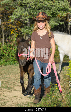 Jeune blonde cowgirl menant son cheval miniature, smiling girl de 13 ans avec de jolis yeux bleus. Banque D'Images