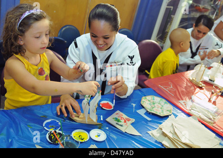 Un marin de l'US Navy participe à un événement de sensibilisation communautaire Caps for Kids, aidant un jeune patient de l'hôpital pour enfants de Boston à peindre un modèle de voilier. Banque D'Images