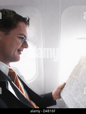 Un homme d'affaires et la lecture de la section des finances d'un journal, dans un avion. Banque D'Images